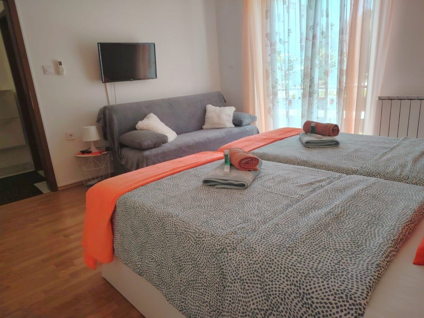Ett hotellrum med två sängar, en platt-TV, ett litet bord med en lampa och ett fönster med gardiner.