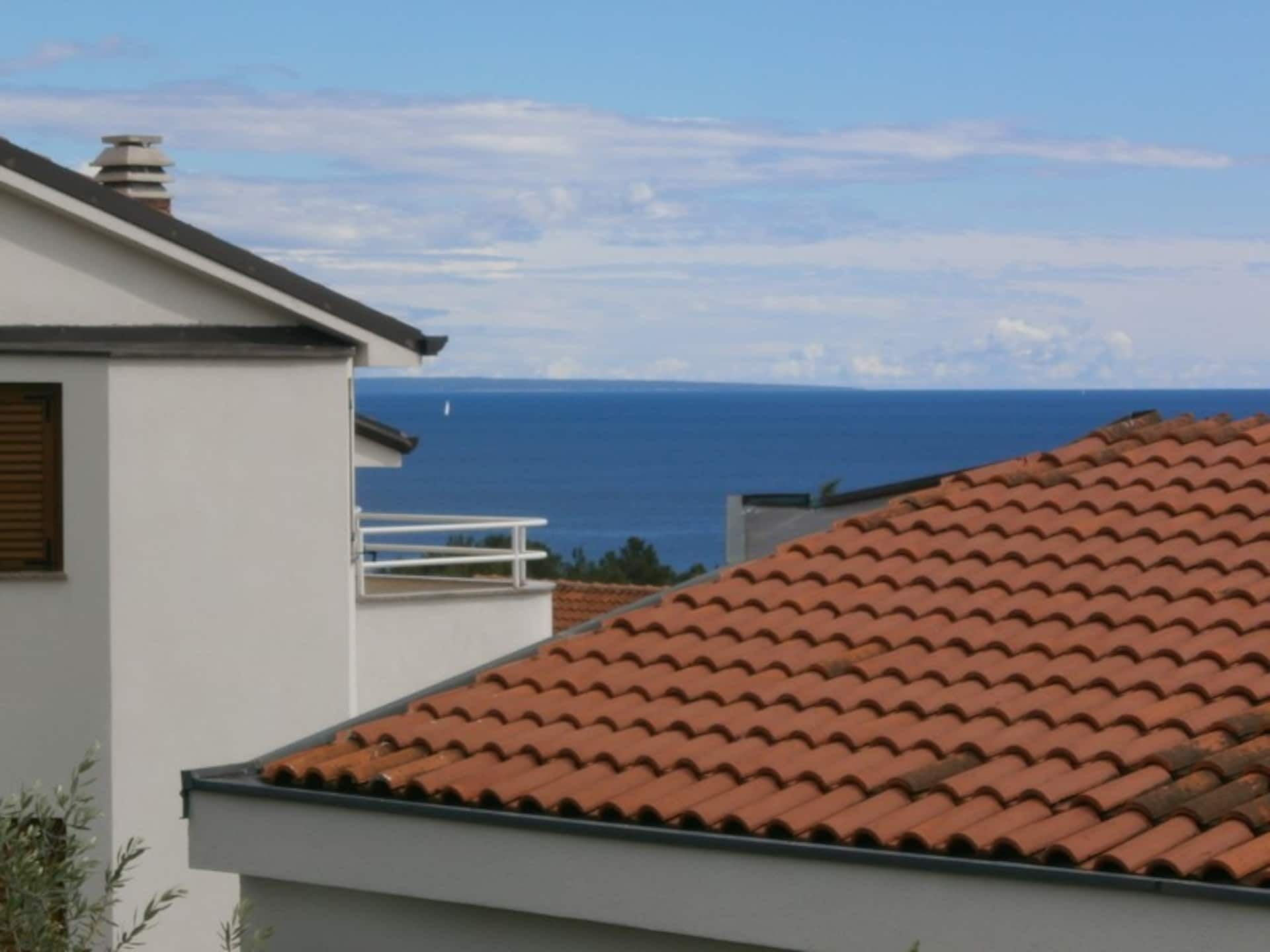 A building with a red-tiled roof and a white exterior wall, overlooking a body of water.
