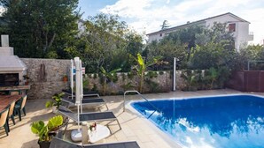 Un área de piscina con sillones de descanso, una parrilla y plantas en macetas.