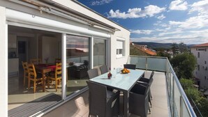 Un balcón con una mesa y sillas de vidrio, vistas del entorno y una puerta que da a un espacio interior.