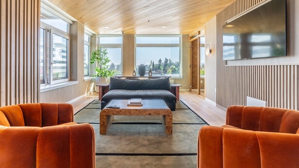 A modern living room with a sofa, two armchairs, a coffee table, and a TV mounted on the wall. - 2BR | Gym, Lounge | Bellevue | Sophari Downtown E (Bellevue)