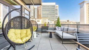 A rooftop terrace with wicker chairs, a sofa, and a small table. - 2BR | Gym, Lounge | Bellevue | Sophari Downtown E (Bellevue)