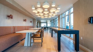 A spacious indoor area with a pool table, seating, and large windows. - 2BR | Gym, Lounge | Bellevue | Sophari Downtown E (Bellevue)
