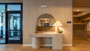A hotel reception area with a counter, a mirror, a lamp, and a sign indicating mail and small package lockers. - 2BR | Gym, Lounge | Bellevue | Sophari Downtown E (Bellevue)