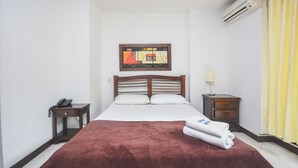 Ein Hotelzimmer mit Bett, Nachttisch mit Lampe, Wandklimaanlage und Vorhang.