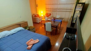 Habitación de hotel con cama, escritorio, silla, televisión y una mesita.