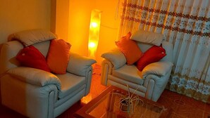 Una sala de estar con dos sillones, una mesa de centro de vidrio y una lámpara de pie.
