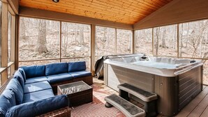 Ein überdachter Außenbereich mit Whirlpool, Holzbalkendecke und großen Fenstern.