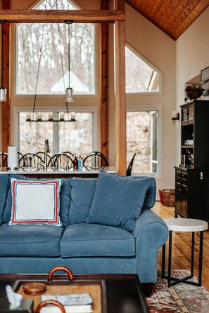 Un salon chaleureux avec un canapé bleu, une table basse en bois et un coin repas comprenant des chaises et un lustre.