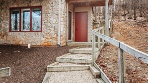 Ein Steinhaus mit roter Tür und Holzstufen, die zu einem überdachten Eingang führen.