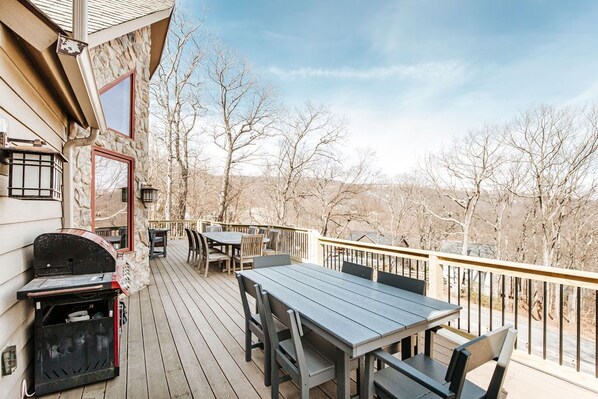 A wooden deck with a table and chairs, a grill, and a stone wall.