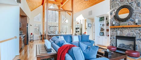 Un salón espacioso con techo de madera, chimenea de piedra y un sofá grande azul.