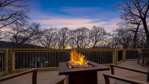 A deck with a fire feature, wooden chairs, and a view of trees and a sunset. - Red White & WTG: Hot Tub, 5 Bedrooms! (Wintergreen Resort)
