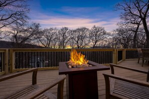 Una terraza con una chimenea, sillas de madera y vistas a árboles y un atardecer.
