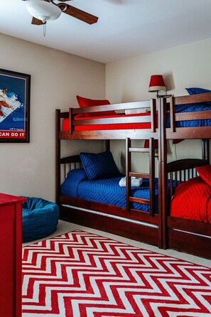 Habitación con literas, ventilador de techo, un cartel en la pared y una alfombra estampada.