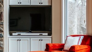 Ein Wohnzimmer mit einem großen Flachbildfernseher, weißen Schränken, einem roten Sessel und einem gemusterten Teppich.