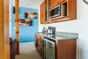Une cuisine compacte avec des meubles en bois, un four à micro-ondes et un réfrigérateur. Le mur bleu est décoré de peintures abstraites.