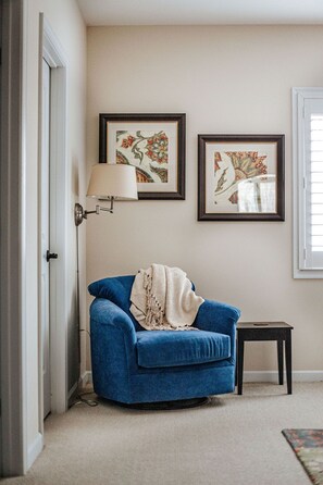 A room with a blue sofa, a small table, a lamp, and two framed pictures on the wall.
