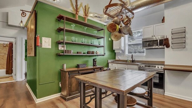 Una cocina con paredes verdes, estantes de madera y una mesa central.