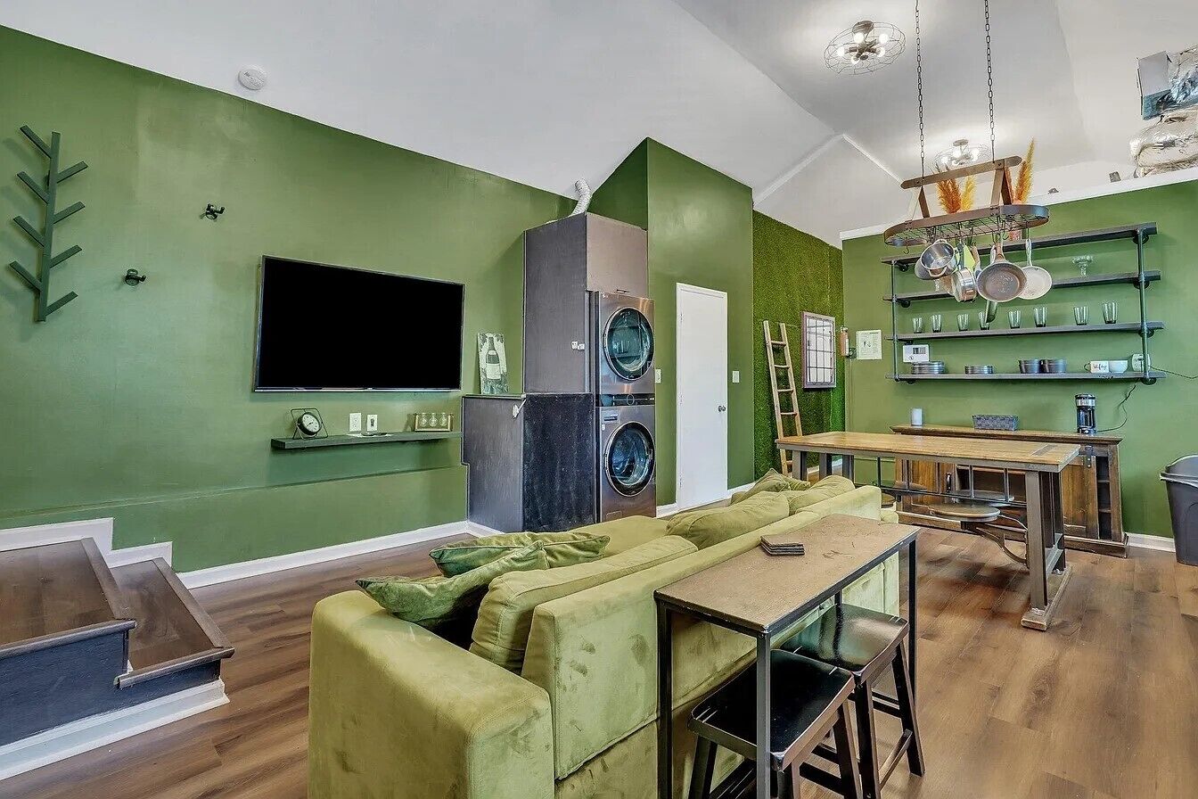 Ein grüner Wohnraum mit einer Couch, Fernseher und einem Essbereich mit Tisch und Stühlen.