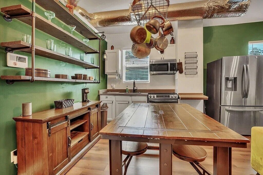 Cozinha com armários de madeira, uma mesa grande de madeira e eletrodomésticos de aço inoxidável.
