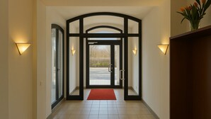A hotel entrance with a red carpet, glass doors, and wall-mounted lights. - Hotel Villa Noel – Central Station Dresden (Dresden)