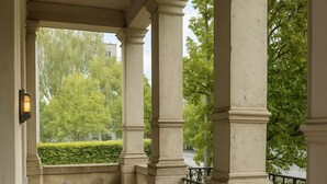 A covered outdoor seating area with two chairs and a small round table, surrounded by columns and a wrought iron railing. - Hotel Villa Noel – Central Station Dresden (Dresden)