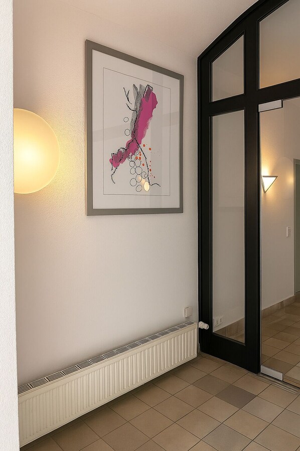 A hallway with a framed abstract artwork on the wall, a radiator below, and a sliding glass door leading to another room. - Hotel Villa Noel – Central Station Dresden (Dresden)