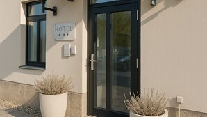 A hotel entrance with a black door, a covered entrance, and two large potted plants. - Hotel Villa Noel – Central Station Dresden (Dresden)