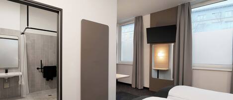 Habitación de hotel con cama, baño, televisión y ventana con cortinas.