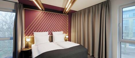 A hotel room with a bed, bedside tables, a window, and curtains.