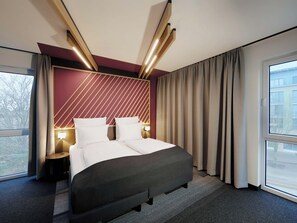 A hotel room with a bed, bedside tables, a window, and curtains. - B&B HOTEL Frankfurt-Oder (Frankfurt an der Oder)