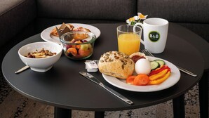 En frukostuppsättning på ett runt bord med en skål med flingor, ett glas apelsinjuice, en tallrik med ägg och grönsaker samt en muffin.