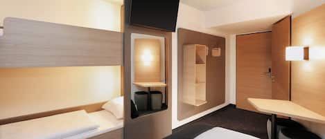 Una habitación de hotel con una cama, una mesita de noche, un espejo, un estante en la pared y una puerta.