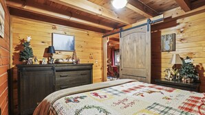 Une chambre confortable dans un chalet en rondins, avec un lit en bois, une commode, un petit sapin de Noël et une cheminée.