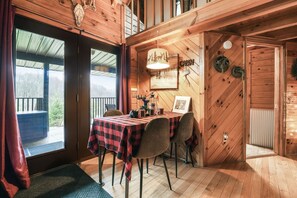 A wooden cabin interior with a dining table, chairs, and a view through the glass door. - Buck Ridge | Hocking Hills, Rustic Cabin, Hot Tub (Laurelville)