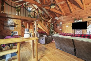 Ein gemütliches Cabin-Interieur mit einer Holztreppe, einem Kamin, einem Flachbildfernseher und Weihnachtsdekorationen.