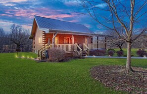 A log cabin with a porch, surrounded by a well-maintained lawn and trees. - Buck Ridge | Hocking Hills, Rustic Cabin, Hot Tub (Laurelville)