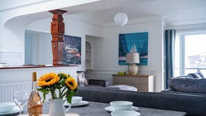 A modern living room with a sofa, a dining table set with plates and a wine bottle, and a painting on the wall. - Breathtaking 180° Ocean Views (Ventnor)