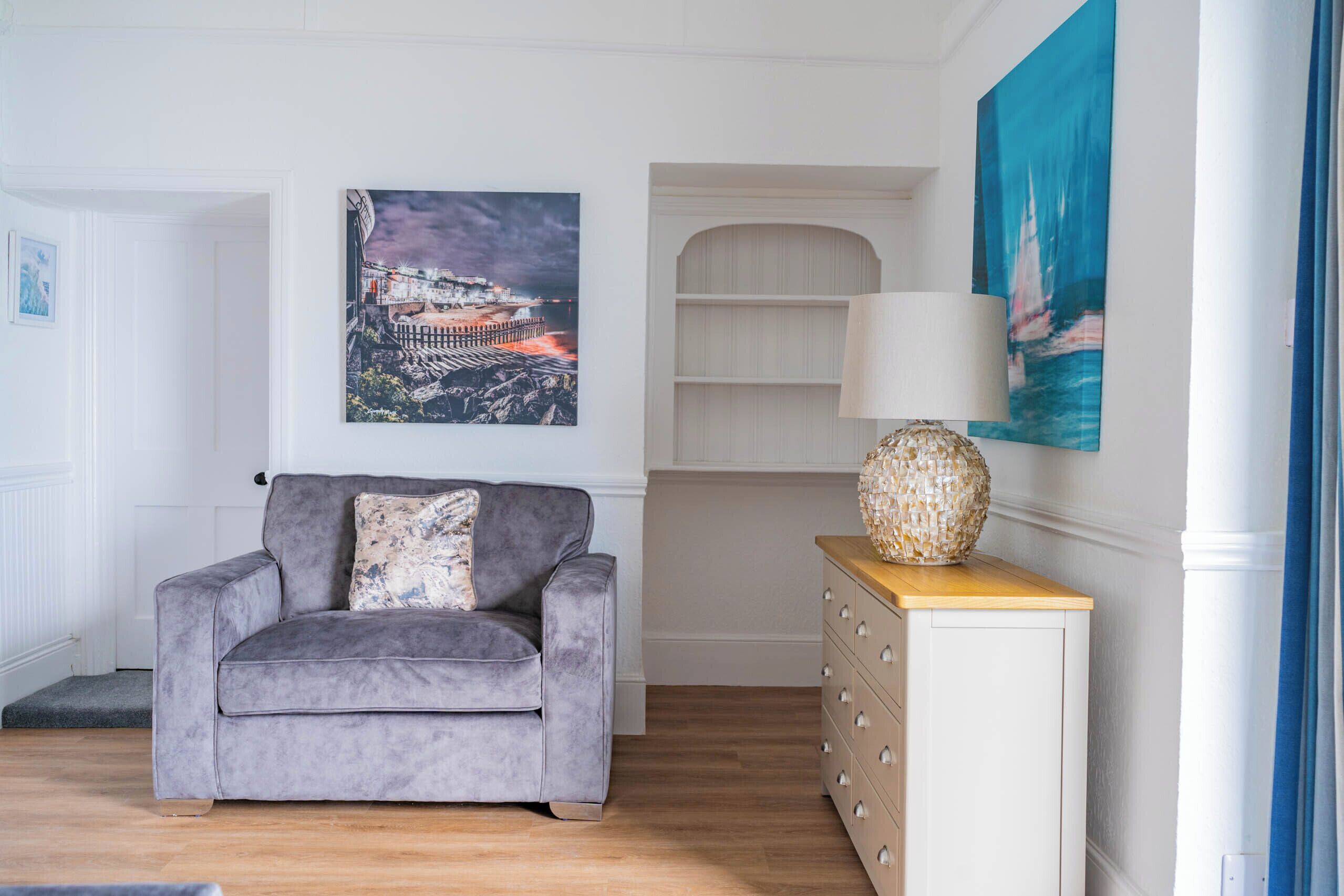 A living room with a grey sofa, a wooden cabinet, and a wall-mounted lamp.