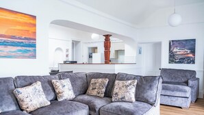 A modern living room with a grey sectional sofa, a grey armchair, and a wooden column. - Breathtaking 180° Ocean Views (Ventnor)