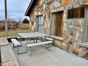 Un bâtiment en pierre avec une table de pique-nique et des bancs à l’extérieur.