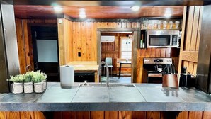 Una cocina con paredes de madera, una isla central, microondas, horno y un lavamanos.