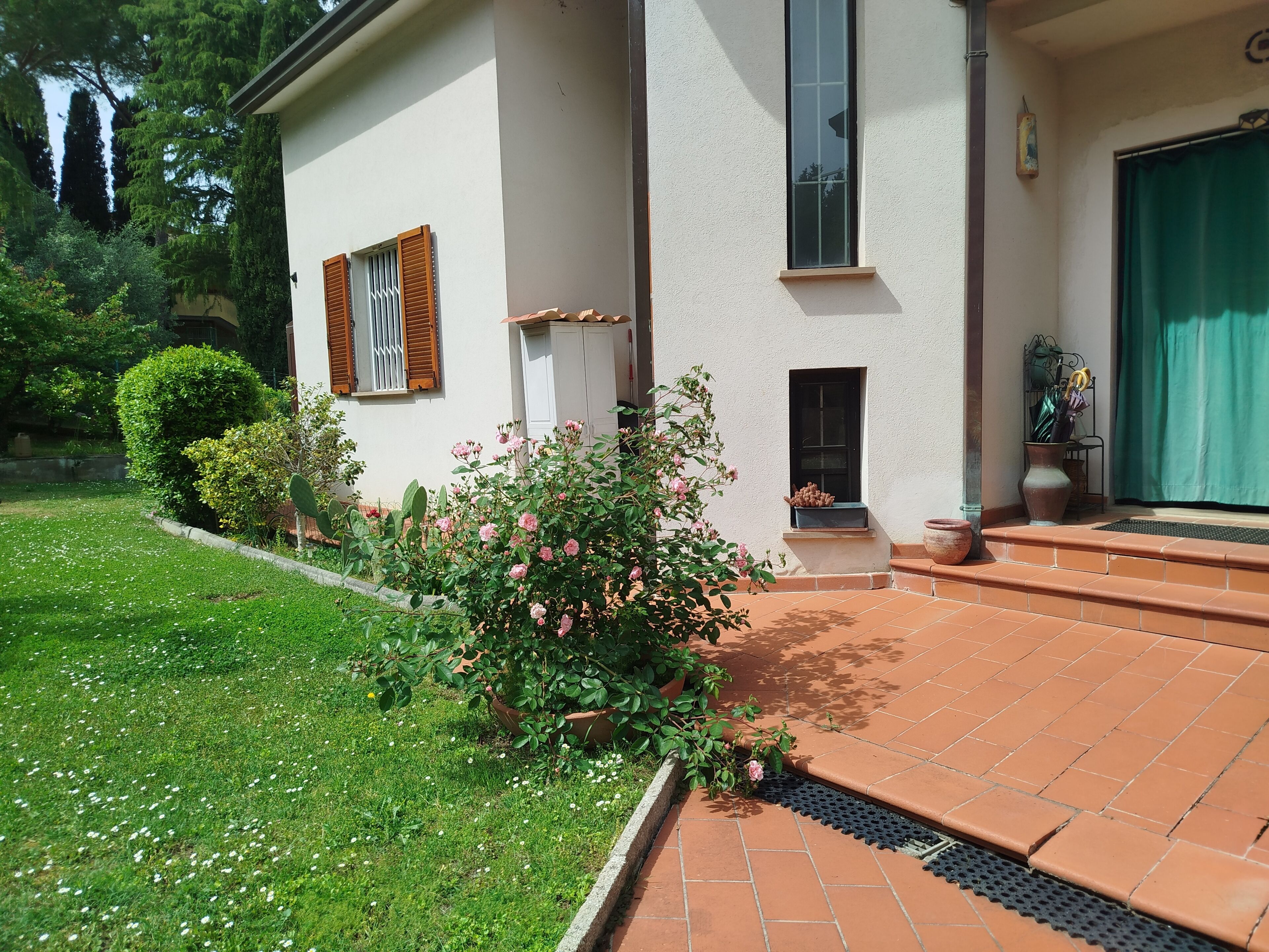Une maison avec un patio carrelé, un petit jardin agrémenté de fleurs roses et un mur extérieur blanc.
