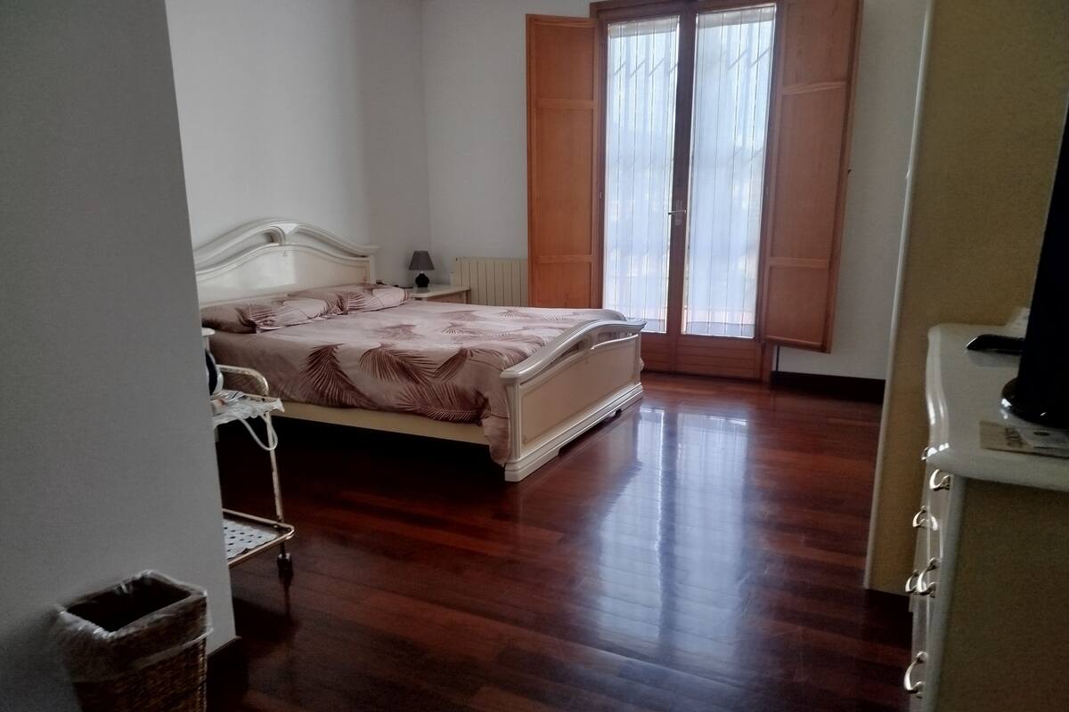Ein Schlafzimmer mit Bett, Nachttisch, Lampe, einem Fenster mit Vorhängen und Holzboden.