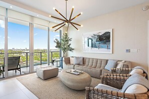 A modern living room with a large window, a unique ceiling light, a comfortable sofa set, and a framed picture on the wall.