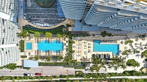 A hotel with two large swimming pools, sun loungers, and palm trees.
