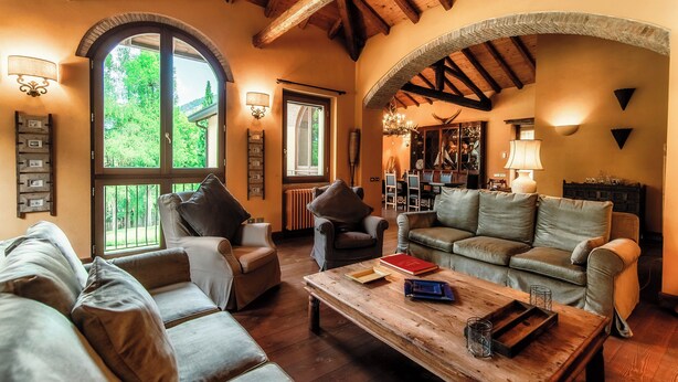 A spacious living room with a wooden ceiling, large windows, and a fireplace. - Villa Oasi (Canzo)