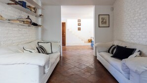 Ein Wohnzimmer mit zwei weißen Sofas, einer weißen Ziegelwand und einer Treppe, die zu einem anderen Raum führt.