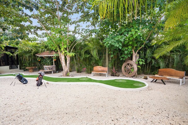 A garden with a gravel path, benches, a wooden wheel, and a small table.